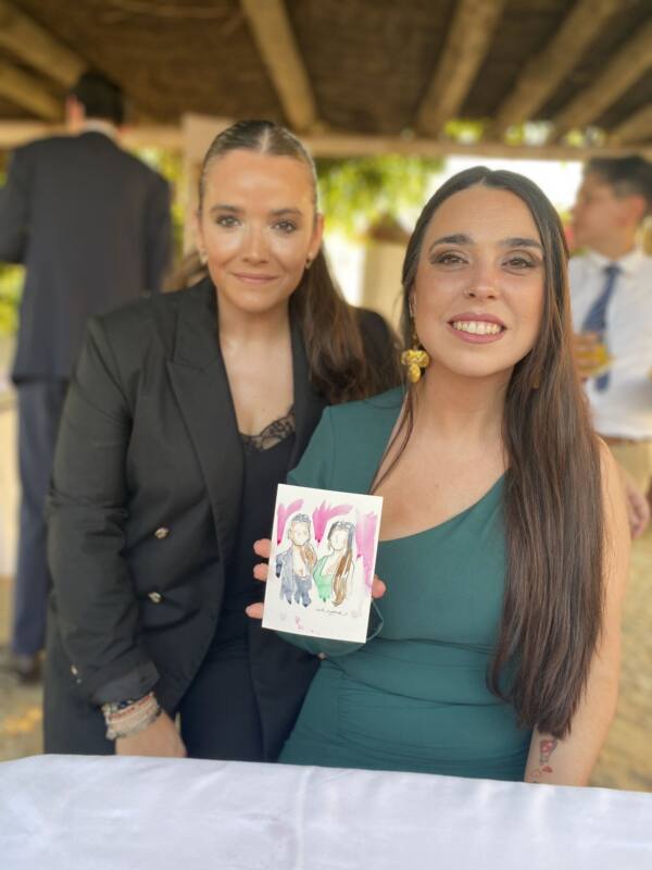Dos invitadas enseñando el retrato en acuarela que se llevan de la boda