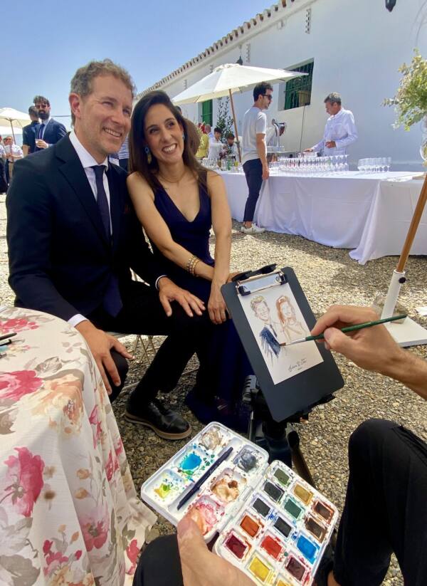 Pareja de invitados posando mientras Alberto Jurada pinta su retrato en acuarela
