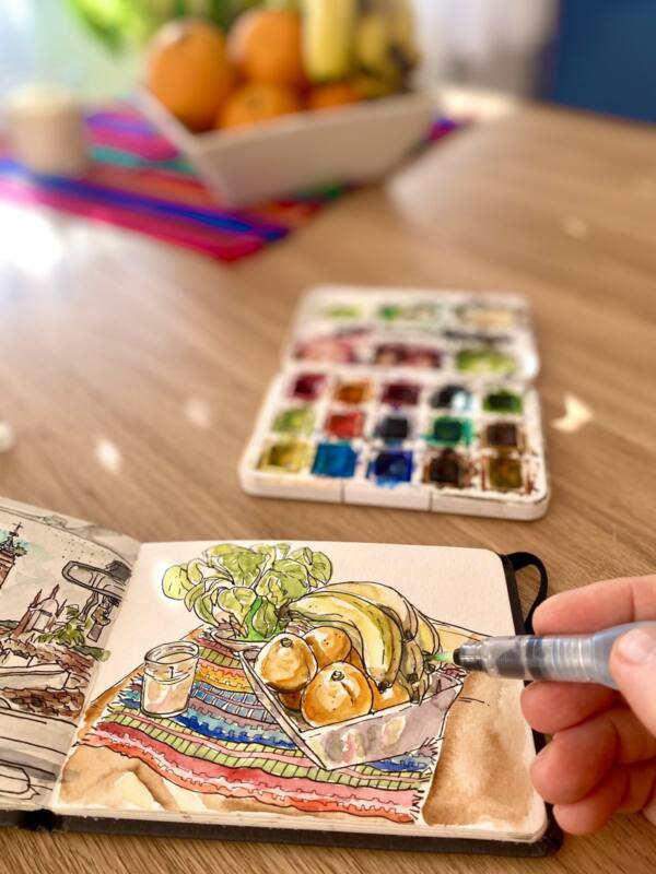 Alberto Jurada pintando un bodegón de fruta en su cuaderno, con el frutero al fondo