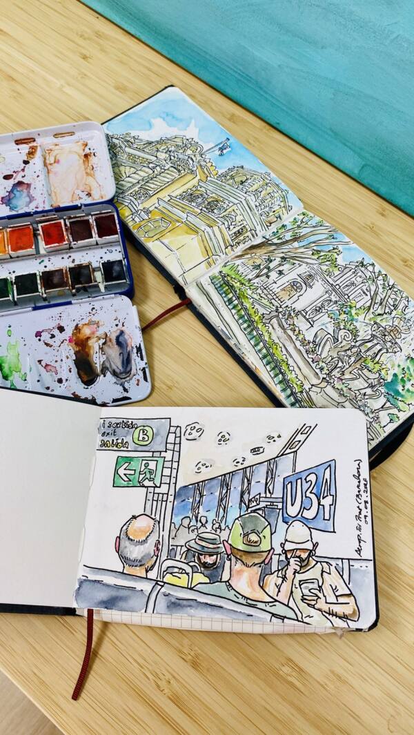 Dos cuadernos de viaje abiertos junto a una caja de acuarelas sobre la mesa del estudio