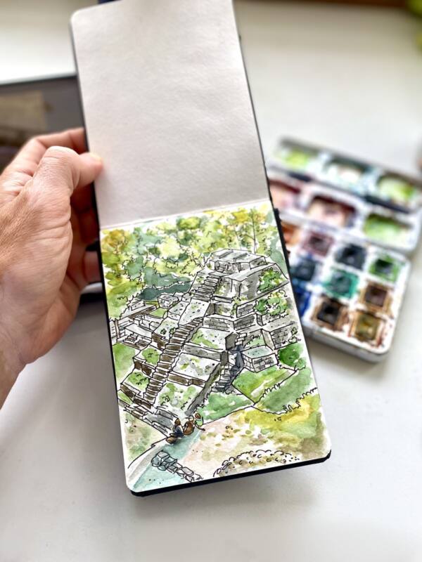 Cuaderno de viaje con la acuarela de la pirámide de Yaxhá junto a la caja de acuarelas