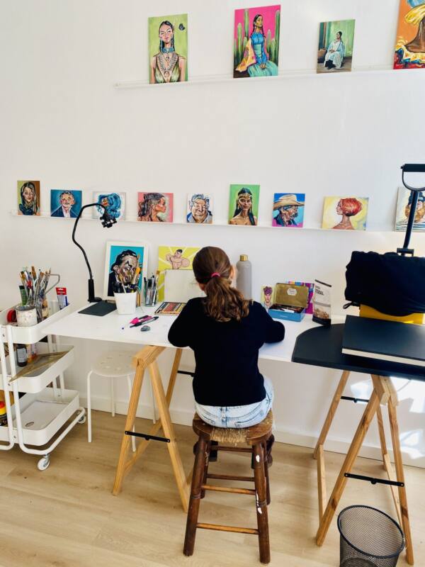 Niña dibujando en una mesa de trabajo del estudio, bajo los retratos de la pared