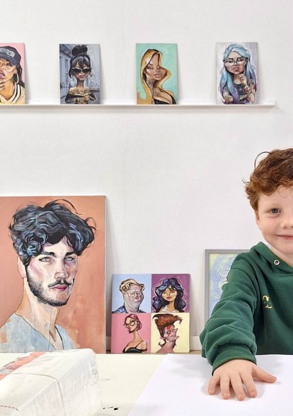 Niño sonriendo junto a los retratos pintados del estudio