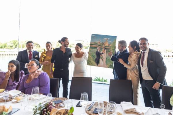 Novios e invitados celebrando junto al cuadro pintado en directo a orillas del río