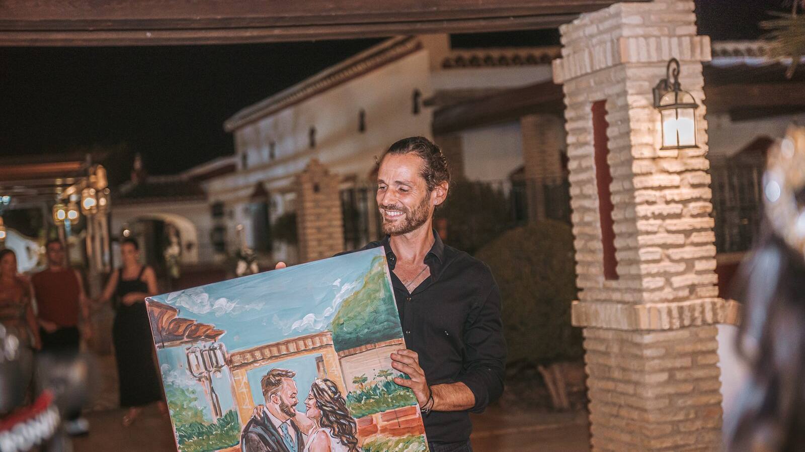 Alberto Jurada sonriendo con el cuadro de los novios recién terminado en la boda