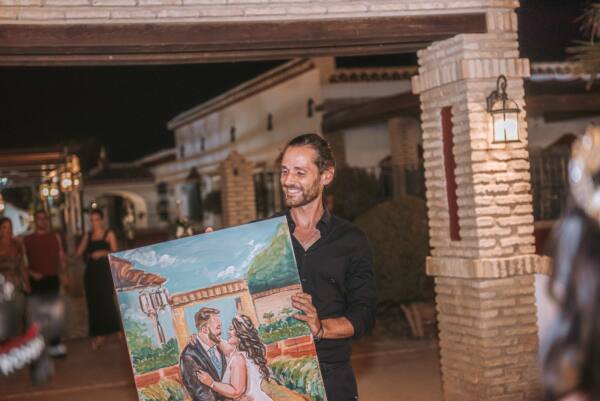 Alberto Jurada sonriendo con el cuadro de los novios recién terminado en la boda