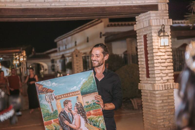 Alberto Jurada sonriendo con el cuadro de los novios recién terminado en la boda