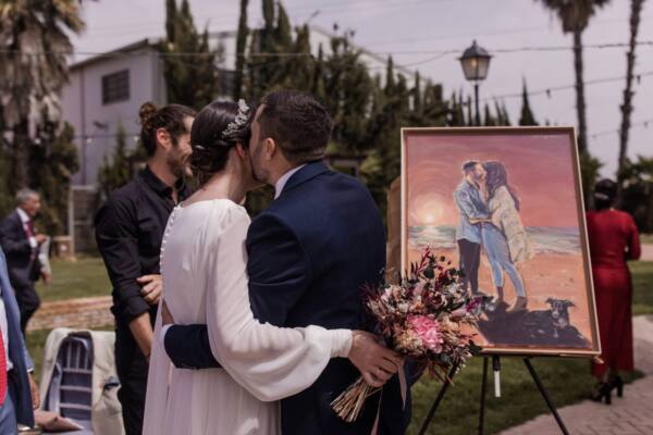 Novios besándose junto al cuadro de su atardecer pintado en directo