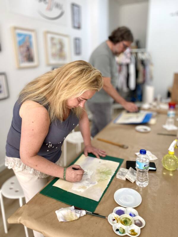 Alumna pintando una acuarela de pie junto a la mesa del taller
