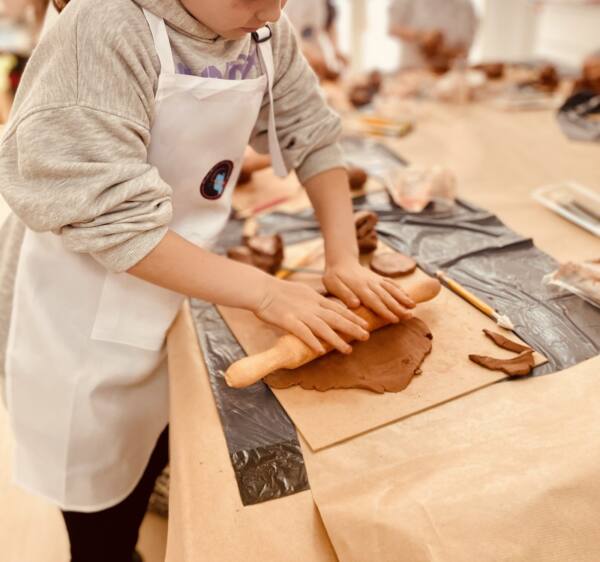 Niño estirando barro con un rodillo en el taller de barro