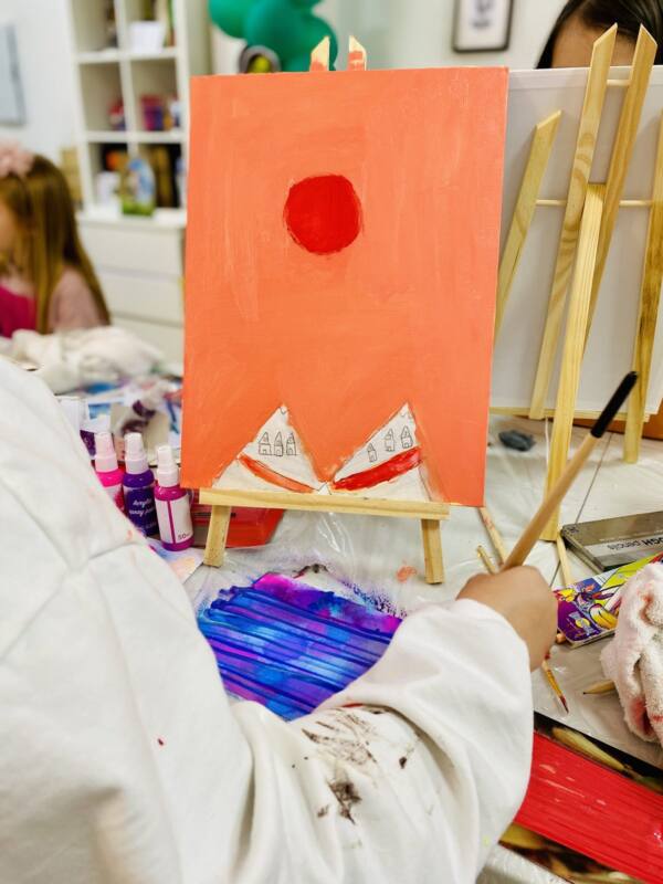 Niña pintando un lienzo naranja en el taller infantil