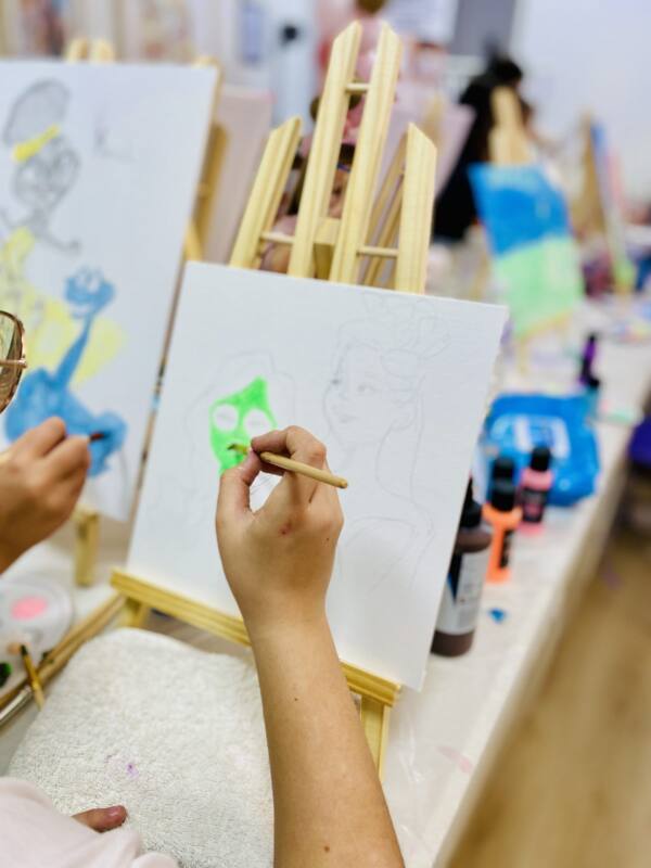 Manos pintando un retrato en un caballete durante un taller infantil