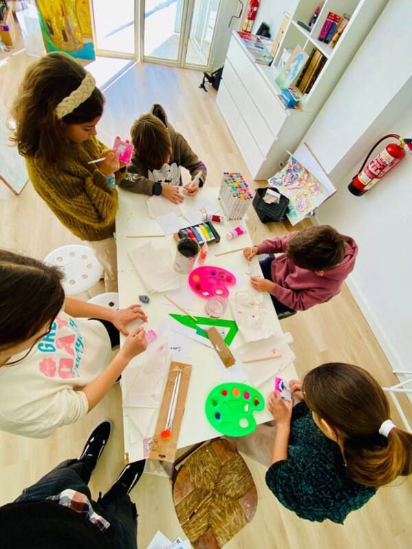 Niñas pintando alrededor de una mesa con paletas de colores en el estudio
