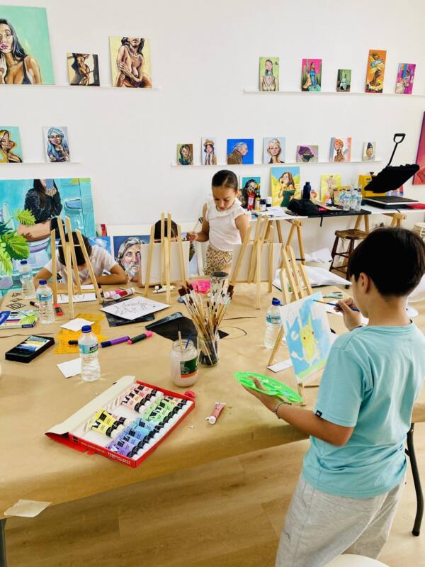 Niños pintando en caballetes en el estudio, con retratos colgados en la pared